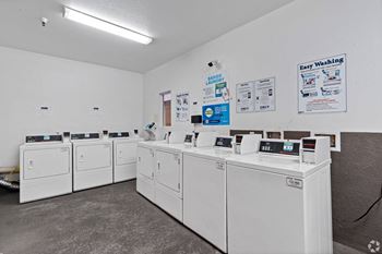 A row of washers and dryers in a laundromat with white machines